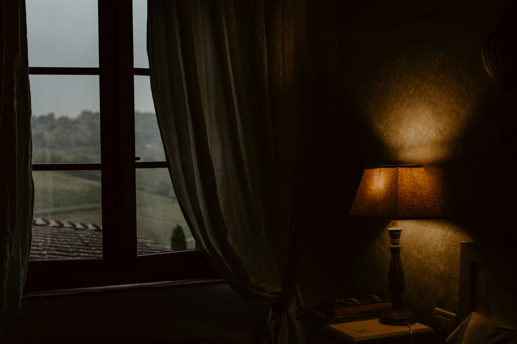 A lamp-lit room at dusk with a view over open countryside